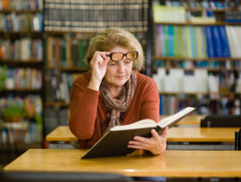 Woman in library lifting glasses to read small print